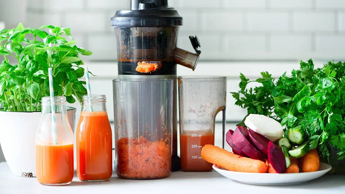 Extracteur de jus avec recipient de pulpe de carotte visible a cote de bouteilles de jus fraiches