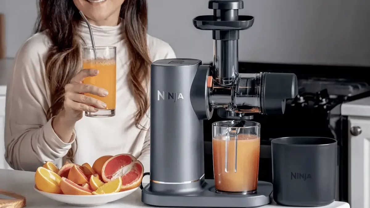 Utilisatrice buvant un jus de pamplemousse à côté d'un extracteur gris