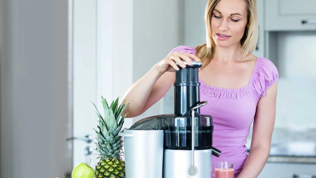 Utilisatrice pressant un ananas dans un extracteur de jus vertical blanc de conception classique