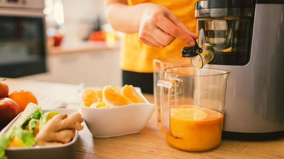 Main versant des quartiers d'orange presses dans un pichet de jus depuis un extracteur